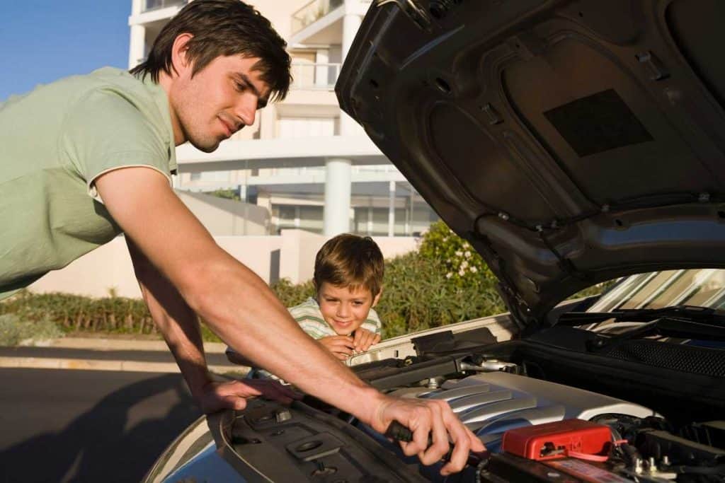 A man fixes his car while his son watches